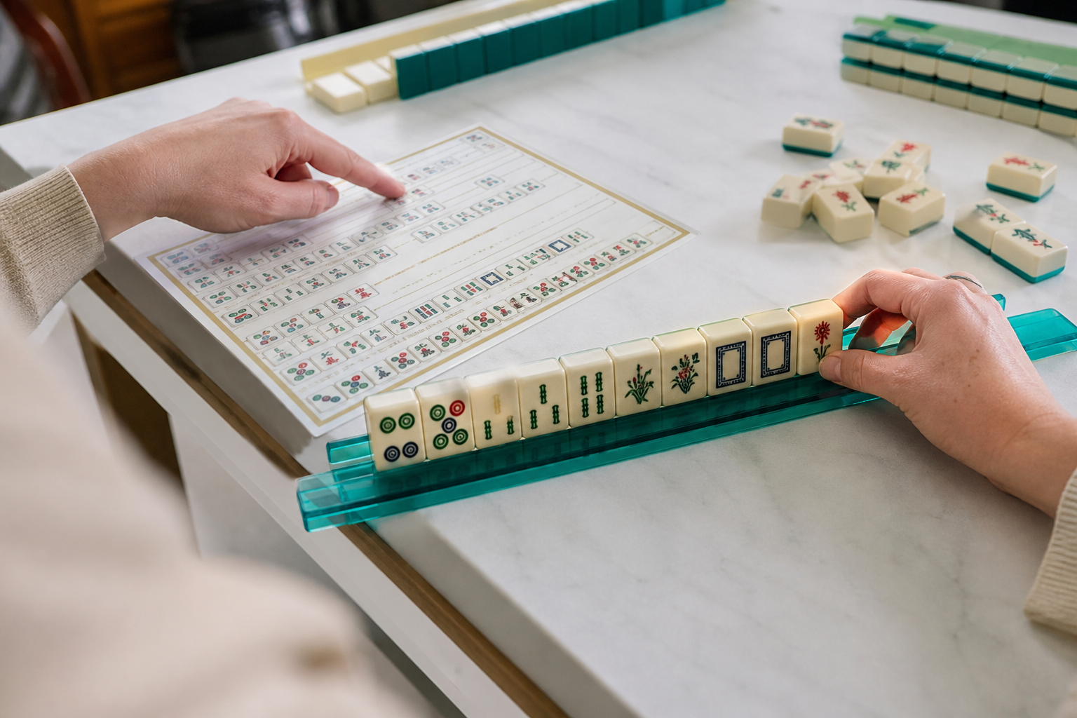 Beginner reading a Mahjong reference card beside a tile rack